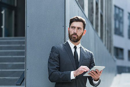正规商业诉讼案中名状有胡子的时髦商务人士 手拿着平板电脑工作男性成功经理金融街道手机管理人员城市职业员工图片