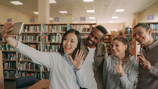 一群国际学生在大学图书馆的智能手机相机上开心地笑着自拍 快乐的朋友在一起进行预项目时休息媒体社交乐趣团队女性成人女孩书架友谊鬼脸图片