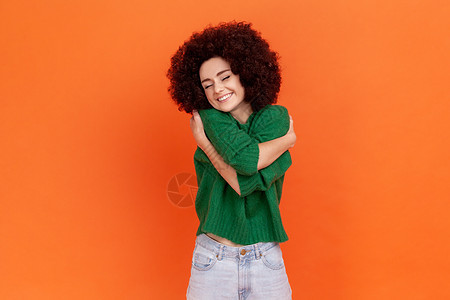 穿着绿色休闲毛衣 留着非洲发型的女人拥抱着自己 微笑着 感到舒适和满足 自恋的利己主义者图片