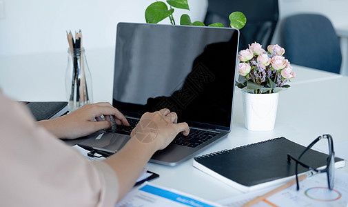 一位在办公室用笔记本电脑空白黑屏工作的女商务人士的侧面视图图片