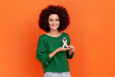 满意的善良女人 留着非洲式发型 穿着绿色休闲风格的毛衣 上面有粉色丝带 象征着女性健康 癌症图片