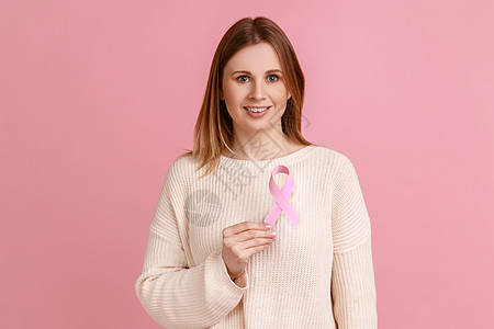微笑的妇女站在胸前握着粉色丝带 乳腺癌 妇女健康概念等 并站立不动图片