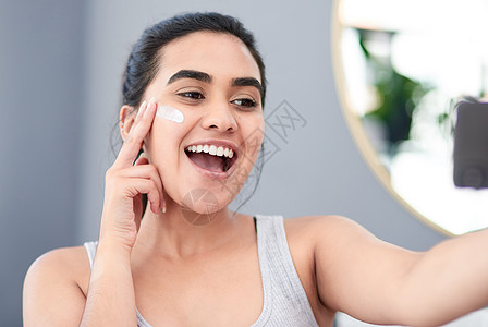 好的化妆应用的第一条规则是好的护肤品 美丽的年轻女子兴高采烈地用新润肤霜拍下她的脸图片