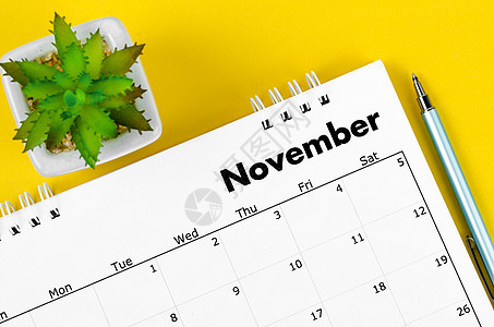 2022年11月的案头日历和笔 还有黄色背景的植物锅图片