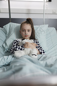 生病的小女孩在接受治疗时身着氧气管 同时拿着肥肉熊玩具背景图片