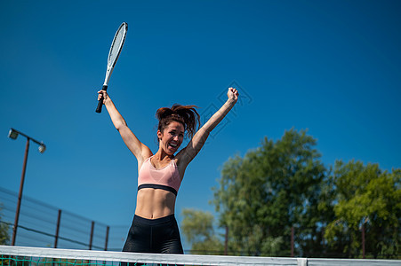 女胜者庆祝她的网球成功 快乐的女孩在户外网球场上跳跃手势女士情感球拍游戏爱好运动服法庭运动闲暇图片
