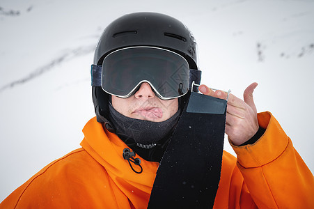 一个年轻的滑雪运动员在冬天站在山坡上 展示他的舌头图片