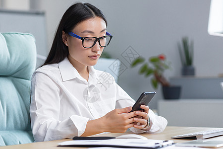 一位戴眼镜的亚洲女商务人士手里拿着电话 拨打一个信息 笑声技术办公室商务工作公司微笑测试阅读管理人员讨论图片