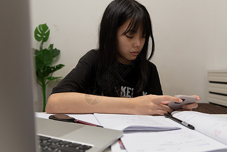 亚裔女学生在书桌上写家庭作业和阅读书教育桌子专注童年房间瞳孔课堂大学女孩考试图片