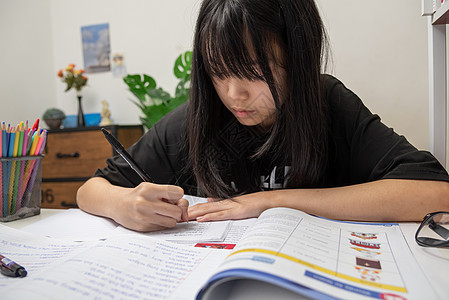 亚裔女学生在书桌上写家庭作业和阅读书教科书班级学校大学绘画专注蜡笔学生童年家庭作业图片