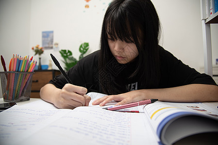 亚裔女学生在书桌上写家庭作业和阅读书女士桌子青少年知识分子学习蜡笔课堂教科书教育专注图片
