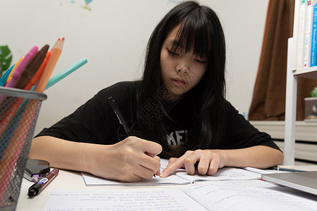 亚裔女学生在书桌上写家庭作业和阅读书测试学习瞳孔知识分子蜡笔考试童年学校绘画班级图片