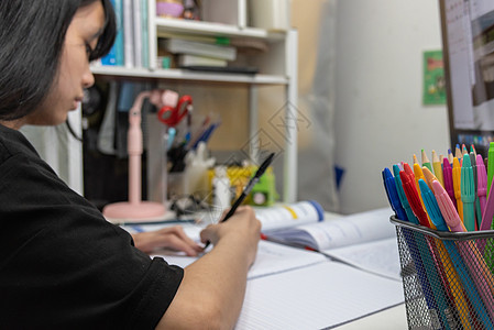 亚裔女学生在书桌上写家庭作业和阅读书大学教育专注蜡笔教科书班级学生思维考试笔记本图片