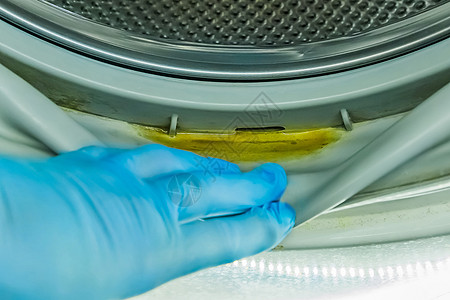 一个戴着橡胶家用手套的男人的手指向洗衣机旧滚筒压实机中的脏水残留气泡合金圆圈烘干机海豹衣服技术涂层家庭器具图片