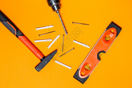 修理家用的工具 钉子锤 水平仪和钻头 橙色背景墙上的销钉 向导工具包螺丝刀装修木匠指甲木工维修房子手套书签金属图片