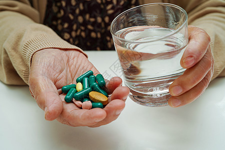 亚洲老年妇女在玻璃杯中拿着药丸 强烈的健康医学理念制药药品医生剂量处方药物药片女性帮助胶囊图片