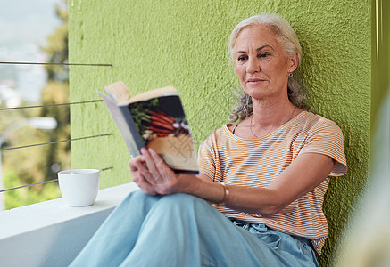 做退休权利 一个成熟的女人读一本书 在家里的阳台上喝咖啡 (笑声)图片