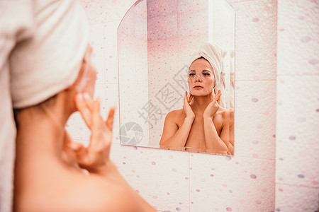 年轻漂亮的女人在洗完澡后使用保湿面膜 头戴毛巾的漂亮迷人女孩站在家庭浴室的镜子前 日常卫生和皮肤护理女性女士化妆品美容奶油粉刺青图片