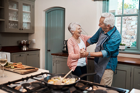 我们知道如何让我们的爱变得坚强 一家老年夫妇在家中厨房做饭时跳着舞背景图片