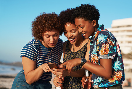 哦 看那张照片 白天 三个迷人的年轻女性挤在一起 在海滩上看手机图片