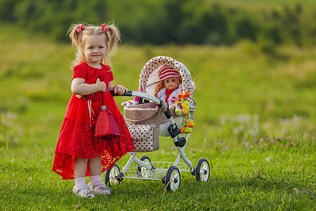 女孩在婴儿车里玩娃娃运输金发游戏母亲微笑快乐婴儿母性季节树木图片