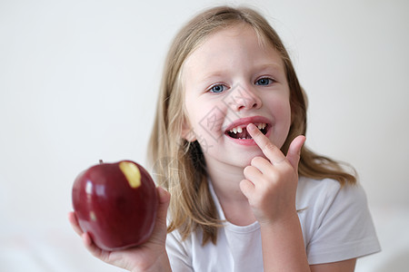 没有牙齿的笑笑可爱女孩 手握着红咬苹果的肖像图片