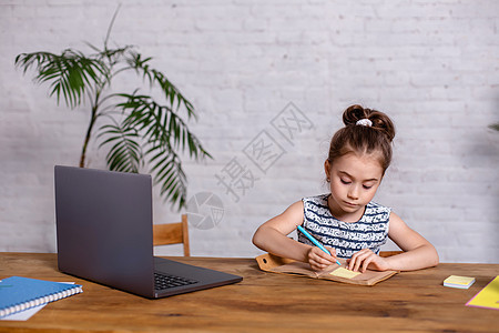 可爱的小女孩坐在桌子上 带着笔记本电脑和笔记本图片