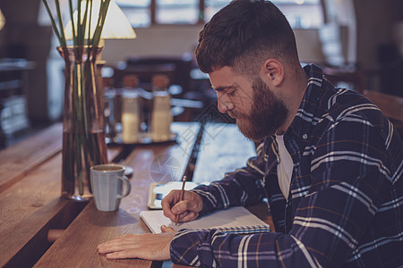 年轻留胡子的商务人士坐在咖啡馆 家在餐桌上写作电子书教育人士成人数据技术阅读商务自由职业者电脑图片