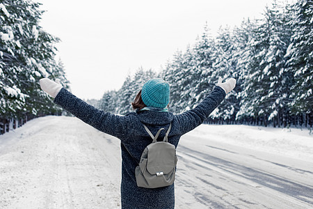 身穿灰色大衣的女孩背着灰色背背包站在路边 在美丽的冬季森林里图片