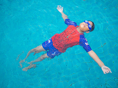 身穿泳衣和眼镜的男孩在游泳池中间游泳 有蓝色水底背景孩子青年游泳者游戏喜悦家庭运动风镜照片气泡图片