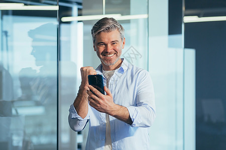 成功的商务人士 为了成功而穿着衬衫的衬衫 拿着一个电话办公室享受灰色胜利赌注商业手机社会技术优胜者图片