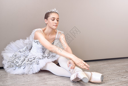 一个可爱的芭蕾舞女郎坐在地板上 双臂伸展向前 在工作室练习芭蕾舞姿势图片