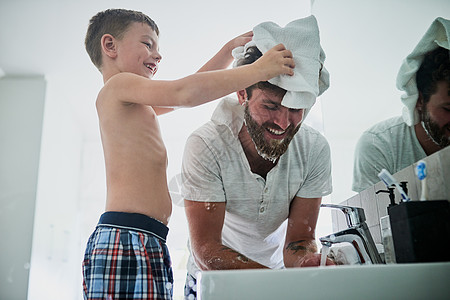 让我来帮你 爸爸 一个小男孩在家中的浴室刮胡子时 给他父亲擦头图片
