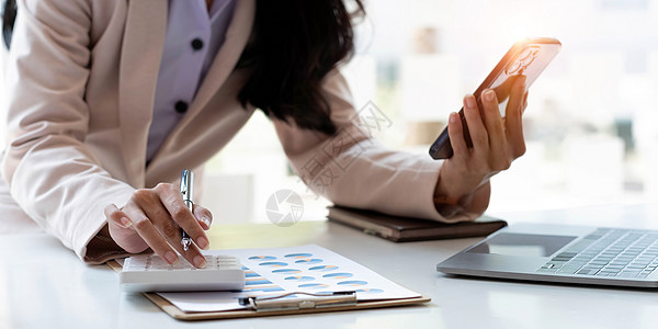 女商务人士或会计手使用计算器 在现代家庭办公室的桌子上使用移动智能手机和笔记本电脑 并在桌子上放上记录数据图表纸 在线营销理念图片