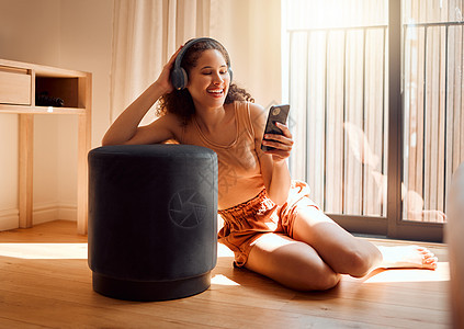 无忧无虑 轻松快乐的女人坐在地板上 用手机和耳机放松视频通话 听在线播客或浏览社交媒体的年轻兴奋女性图片