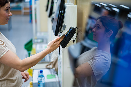 在自检柜台用智能手机买单的女士市场女性电脑零售机器消费者店铺商业电话扫描图片