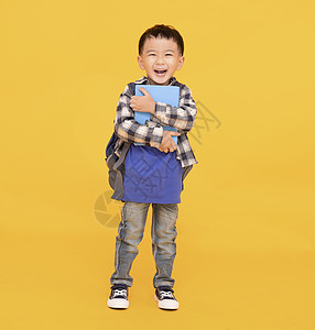 带着或拥抱大本书的亚裔孩子在黄色背景之下欢乐快乐图片