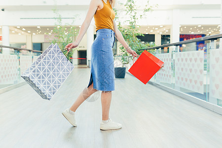 身穿彩色礼品袋的年轻女子在商场走廊走过时的后背风景精品黑色幸福女士销售礼物衣服购物中心喜悦购物狂图片