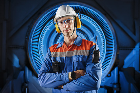 一名年轻专业工程师的肖像 他站在一个戴保护头盔 耳机和眼镜的燃气涡轮发动机旁边图片