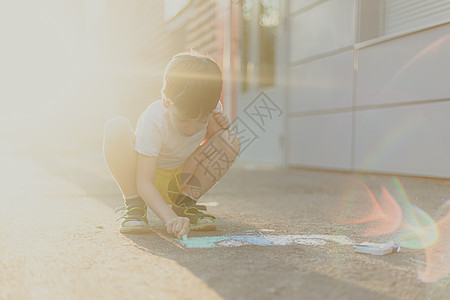 男孩在沥青上画着有蜡笔的生活方式 儿童班 儿童绘画 儿童心理学公园创造力牛仔裤活动粉笔太阳孩子们街道闲暇幸福图片