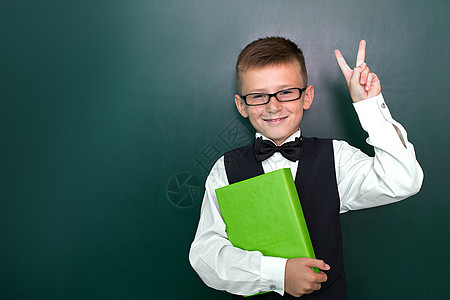 带着领结和眼镜的可爱聪明男孩手握着一本书 第一次上学 回到学校里去黑板男生喜悦幼儿园学生童年女性手指背包男性图片