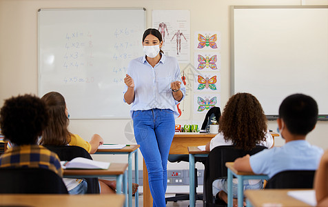 戴口罩的大狗covid 大流行病后的年轻女性教学 在教室里与幼儿学生一起戴着面具 隔离后回到学校 让小孩子从老师那里学习教育背景