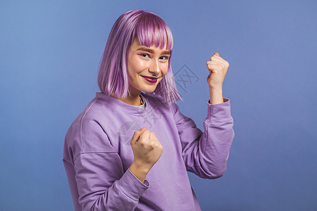 染紫色头发的女人非常高兴和快乐 她展示了胜利的姿态 她取得了成果 目标 紫色工作室背景的惊讶兴奋的快乐女士 头奖概念化妆品女性卷背景图片