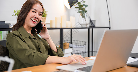 妇女在家庭办公室使用笔记本电脑 同时在移动电话上发言的妇女助手工作电话桌子商务商业营销人士网站命令图片
