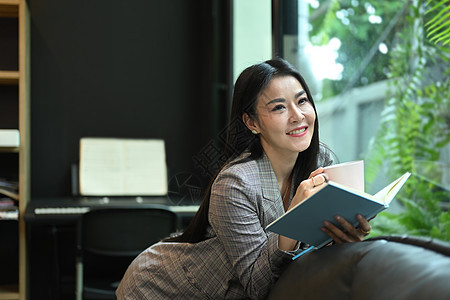 高优雅的亚洲女性商业女商务人士在光亮现代办公室和阅读书中的沙发上躺着图片