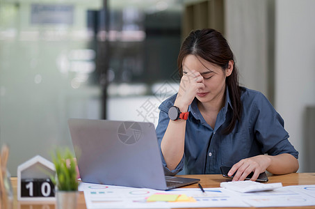 亚洲女性坐在家庭办公室里 压力和眼睛疲劳 疲惫的女商务人士拿着眼镜 按摩鼻梁 有平板电脑 笔记本电脑和咖啡图片