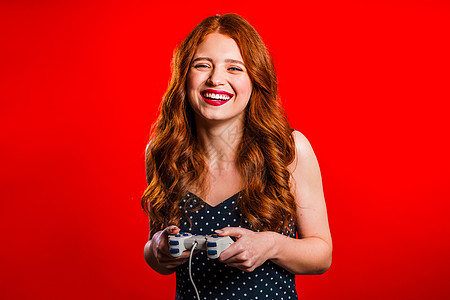 漂亮的年轻女孩在Tv上玩电动刺激游戏 用红色工作室墙壁的摇摆棍 使用现代技术娱乐键盘玩家男性视频手柄电脑闲暇友谊电子游戏图片