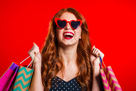 快乐的复古风格年轻女性 在以工作室背景孤立地购物后 带着红色头发和纸袋 季节性销售 购买 花钱买礼物的概念购物者购物中心太阳镜成图片