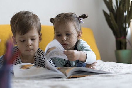 童话书两个学龄前儿童在黄色床上阅读一本有趣的童话故事书 小双胞胎读者的兄弟姐妹在家里隔离时玩得很开心 很开心 友谊 家庭 教育理念派对背景