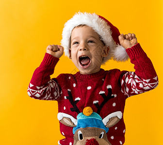 快乐微笑积极快乐积极学龄前小男孩的画像 戴着红色温暖的圣诞老人帽子 在橙色 黄色背景上竖起大拇指 冬季 假日 庆典 圣诞节 新年图片